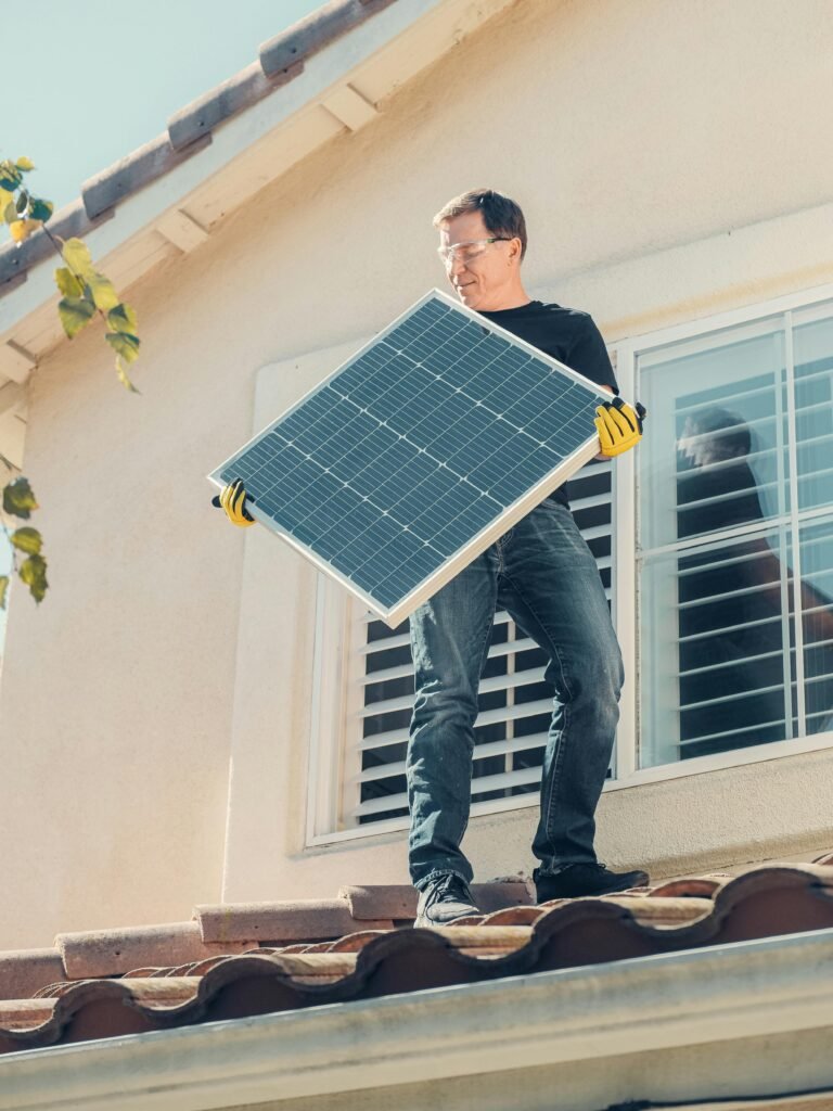 A Man in Black Shirt Standing on the Roof while Holding a Solar Panel